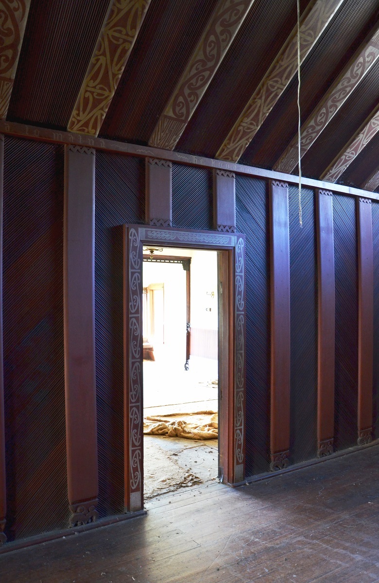 Rehutai hallway. Kōwhaiwhai designs decorated the ridgepole, heke (exposed rafters) and doorways. The bases of the poupou (vertical supports) meeting the heke were carved with tiki heads. Rimu panels were milled to imitate traditional reed linings. Photograph by the author, 2012. All Rights Reserved